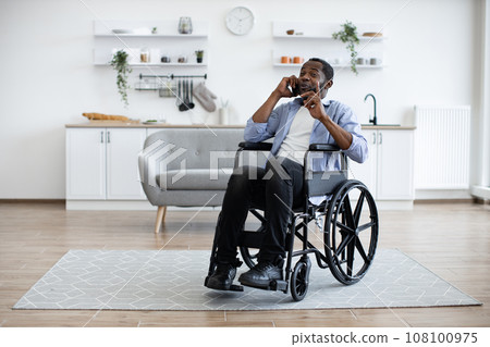 Adult in wheelchair talking on cell phone in studio flat 108100975