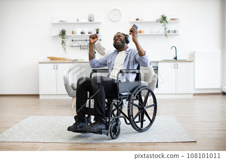 Man in wheelchair and headphones moving hands in air at kitchen table 108101011