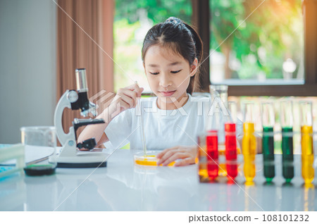 little scientist looking through a microscope and test tubes filled with chemicals for learning about science and experiments. 108101232