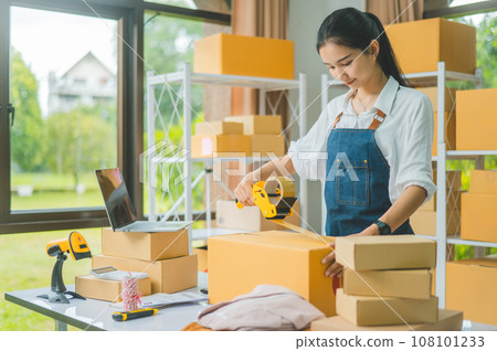 Startup small business owners holding packing machine and sealing cardboard boxes with tape to deliver products to customers- concept shopping online 108101233