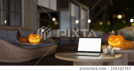 A laptop mockup on a coffee table in an outdoor lounge at night in Halloween theme decor. 108102347