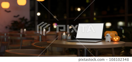 Workspace in Halloween theme with a white-screen laptop mockup on a table in a cafe at night. 108102348