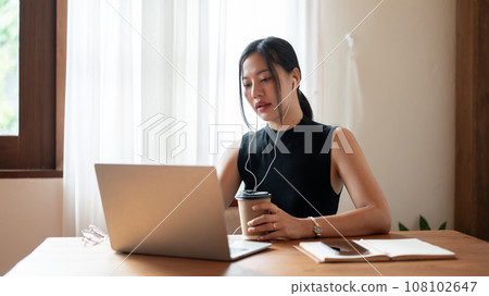 A focused Asian businesswoman is having an online meeting while sitting in a coffee shop. 108102647