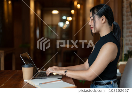Side view of a beautiful Asian businesswoman is working on her laptop in a coffee shop. 108102667
