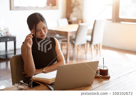 A confident and thoughtful Asian woman is reading online articles while sitting in a coffee shop. 108102672