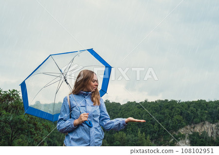 Blonde girl checking the weather under transparent umbrella outside in park. Autumn time rainy bad forecast conditions season. Tourist with umbrella travel in new places in rain Blonde girl checking the weather under transparent umbrella outside in park. Autumn time rainy bad forecast conditions season. Tourist with umbrella travel in new places in rain 108102951