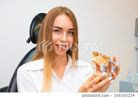 Beautiful dentist in the white lab coat holding a jaw model for study stomatology. Beautiful dentist in the white lab coat holding a jaw model for study stomatology. 108103254