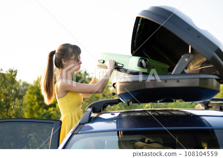 Young woman taking green suitcase from car roof rack. Travel and vacations concept. 108104559