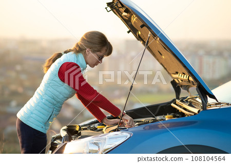 Young woman standing near broken down car with popped up hood having trouble with her vehicle. Young woman standing near broken down car with popped up hood having trouble with her vehicle. 108104564