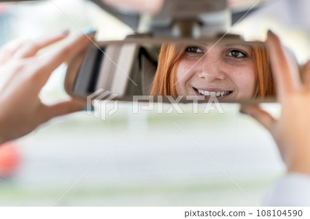 Young woman driver checking rear view mirror looking backwards while driving a car. Young woman driver checking rear view mirror looking backwards while driving a car. 108104590