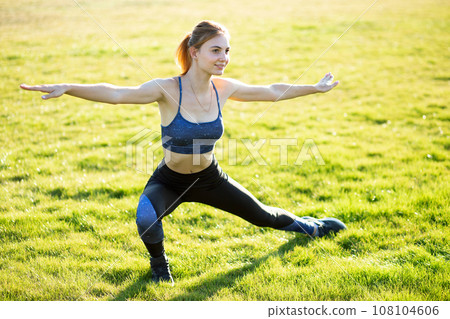 Young sportive woman doing fitness exercises on green grass in warm summer day outdoors. 108104606