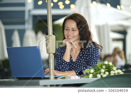 Young happy woman working remotely on laptop computer sitting at outdoor restaurant table. Doing business online concept Young happy woman working remotely on laptop computer sitting at outdoor restaurant table. Doing business online concept 108104659
