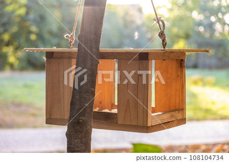 Wooden bird feeder house on a tree in autumn park. Animal wildlife care concept. 108104734