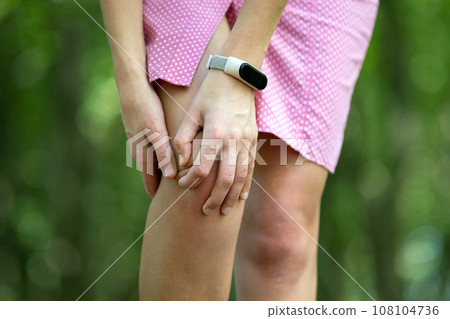 Woman in pink dress holding her knee with hands having cramp pain. Woman in pink dress holding her knee with hands having cramp pain. 108104736