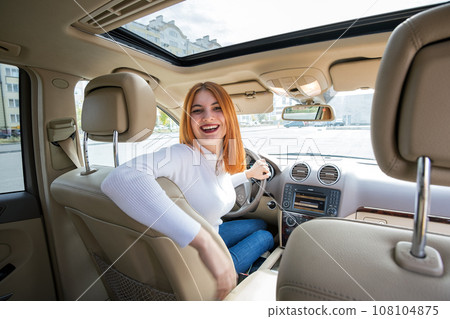 Wide angle view of young redhead woman driver driving a car backwards looking behind. Wide angle view of young redhead woman driver driving a car backwards looking behind. 108104875