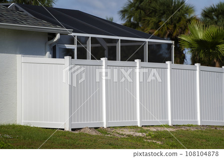 White vinyl picket fence on green lawn surrounding property grounds for backyard protection and privacy 108104878