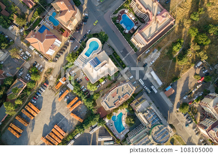 Top down aerial view of hotels roofs, streets with parked cars and swimming pools with blue water in resort city near the sea. 108105000