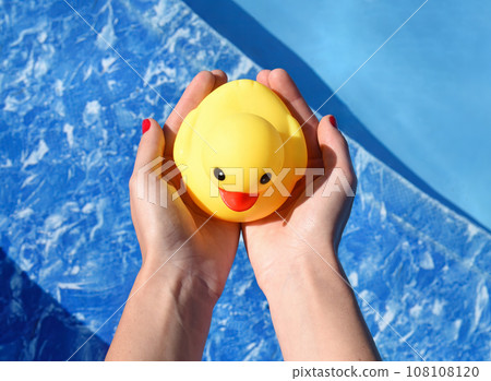 Females hands holding bright yellow rubber duck on pool background Females hands holding bright yellow rubber duck on pool background 108108120