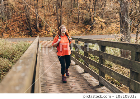 Happy woman hiking in the woods. Hiking active tourist wearing backpack outdoors trekking in autumn forest. 108109332