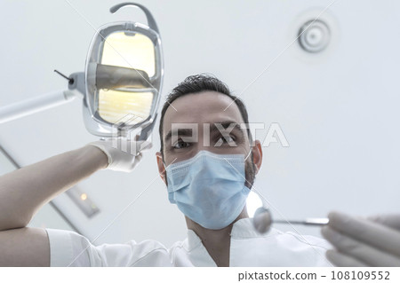 Low angle shot of a male dentist, doing the exam and checking up on oral health of the patient 108109552