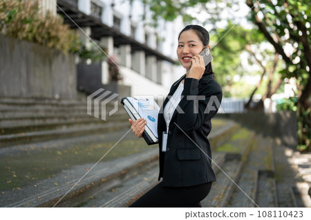 An attractive Asian businesswoman is talking on the phone while walking up the stairs. An attractive Asian businesswoman is talking on the phone while walking up the stairs. 108110423