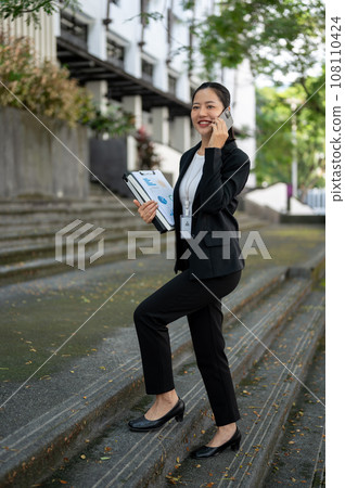 An attractive Asian businesswoman is talking on the phone while walking up the stairs. An attractive Asian businesswoman is talking on the phone while walking up the stairs. 108110424