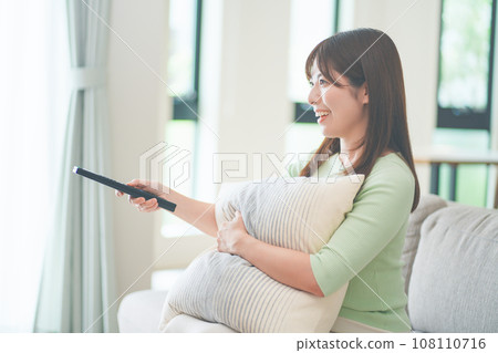一位女士坐在客廳的沙發上操作電視遙控器 108110716