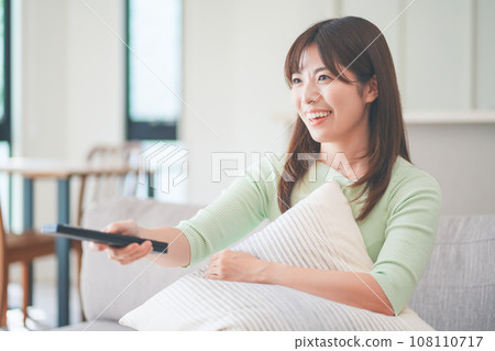 一位女士坐在客廳的沙發上操作電視遙控器 一位女士坐在客廳的沙發上操作電視遙控器 108110717