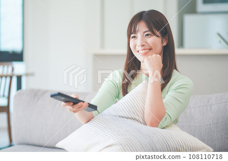 一位女士坐在客廳的沙發上操作電視遙控器 一位女士坐在客廳的沙發上操作電視遙控器 108110718