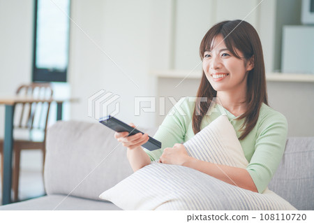 一位女士坐在客廳的沙發上操作電視遙控器 108110720