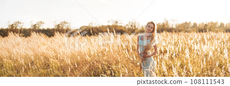 Beautiful blonde woman on a walk in a field with dry grass. A walk in nature, sunset in a field of pampas grass. Beautiful blonde woman on a walk in a field with dry grass. A walk in nature, sunset in a field of pampas grass. 108111543