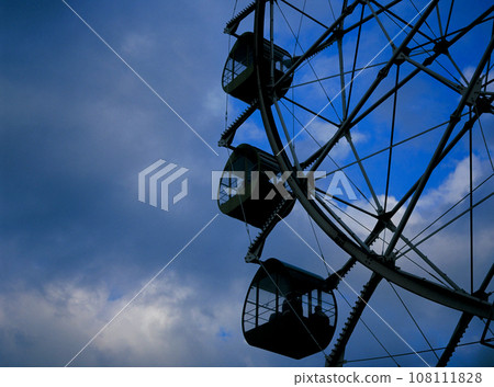 Blue sky and Ferris wheel silhouette visible through thick clouds 108111828