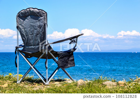 Black folding tourist chair on the background of the Japanese sea without people. with copy space Black folding tourist chair on the background of the Japanese sea without people. with copy space 108112828