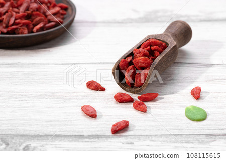 Dried goji berries on wooden spoon and wooden plate on white background. 108115615
