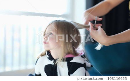 Hairdresser cutting hair of little girl in beauty salon 108116633