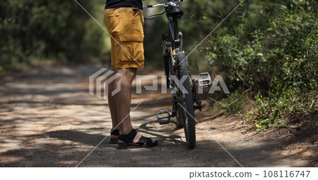 Man standing near mountain bike on path in forest closeup Man standing near mountain bike on path in forest closeup 108116747