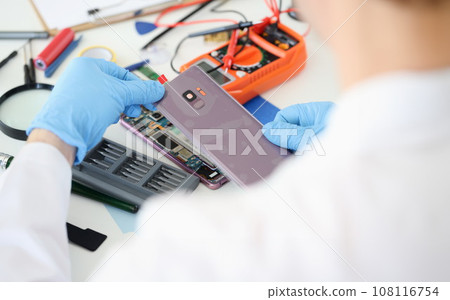 Master opening back cover of mobile phone in workshop closeup 108116754