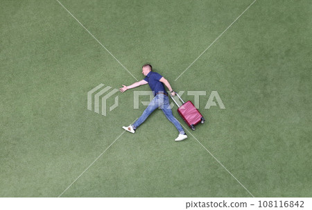 Young man with suitcase walking on green grass top view Young man with suitcase walking on green grass top view 108116842