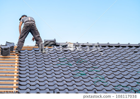 a craftsman on the roof of a bungalow installs a new roof ceramic covering 108117038