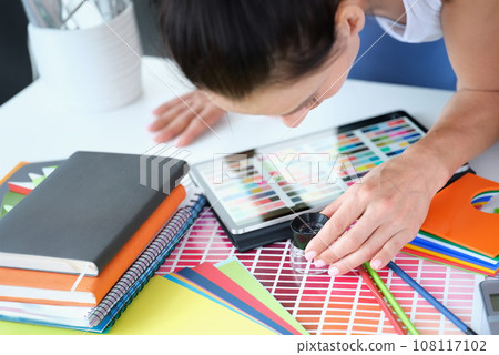 Woman designer looks through magnifying glass at color palette with different shades of colors Woman designer looks through magnifying glass at color palette with different shades of colors 108117102