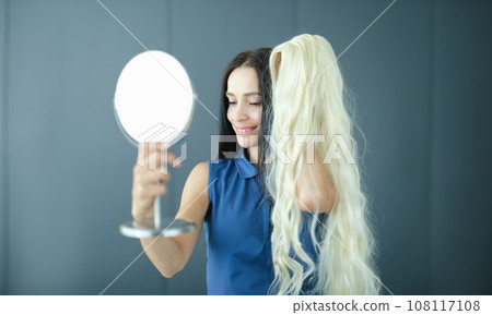 Brunette woman looks in mirror and tries on blonde wig 108117108