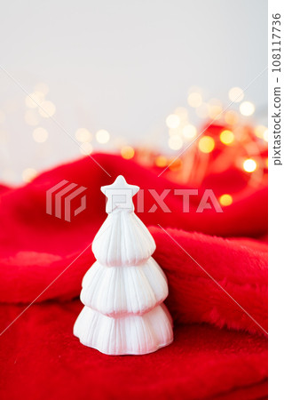 Christmas home interior with a white ceramic Christmas tree on a red blanket. Christmas and New Year concept. Vertical photo. 108117736