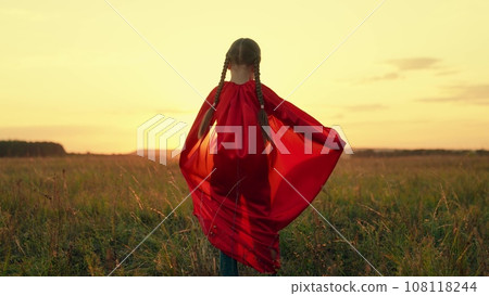 Cute little girl with braids wearing red cloak plays hero in sunset summer meadow 108118244