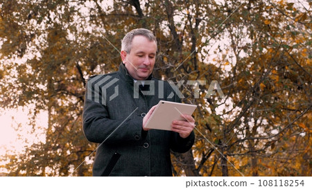 Smiling man prepares presentation on tablet for meeting with workers in park 108118254
