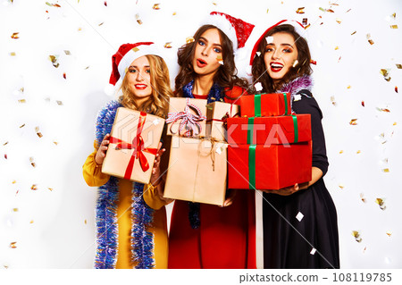 portrait of three happy young women in santa claus hat with gift and sparklers .Christmas concept. portrait of three happy young women in santa claus hat with gift and sparklers .Christmas concept. 108119785