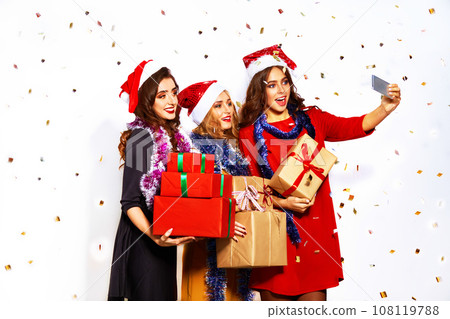 portrait of three happy young women in santa claus hat with gift and sparklers .Christmas concept. portrait of three happy young women in santa claus hat with gift and sparklers .Christmas concept. 108119788