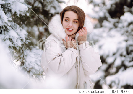 Beautiful woman in winter clothes posing in a snowy park. Young lady walking in a sunny winter day. Beautiful woman in winter clothes posing in a snowy park. Young lady walking in a sunny winter day. 108119824