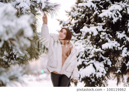 Beautiful woman in winter clothes posing in a snowy park. Young lady walking in a sunny winter day. Beautiful woman in winter clothes posing in a snowy park. Young lady walking in a sunny winter day. 108119862
