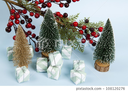 Composition with colorful gifts, a branch of holly with its red berries and christmas tree against a luminous sky-blue background. 108120276