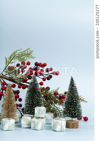 Composition with colorful gifts, a branch of holly with its red berries and christmas tree against a luminous sky-blue background. 108120277